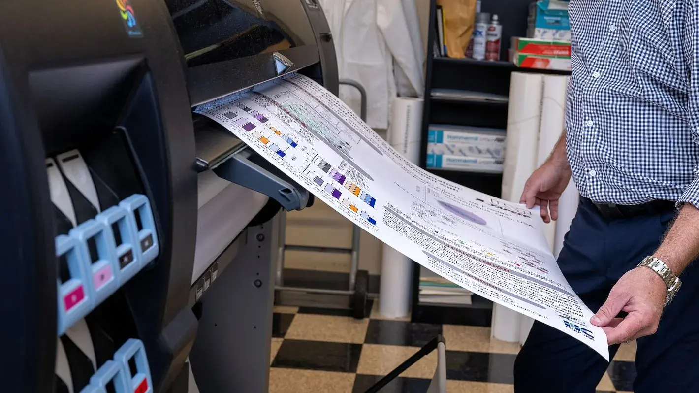 Man holding a large poster that is being actively printed while smiling.