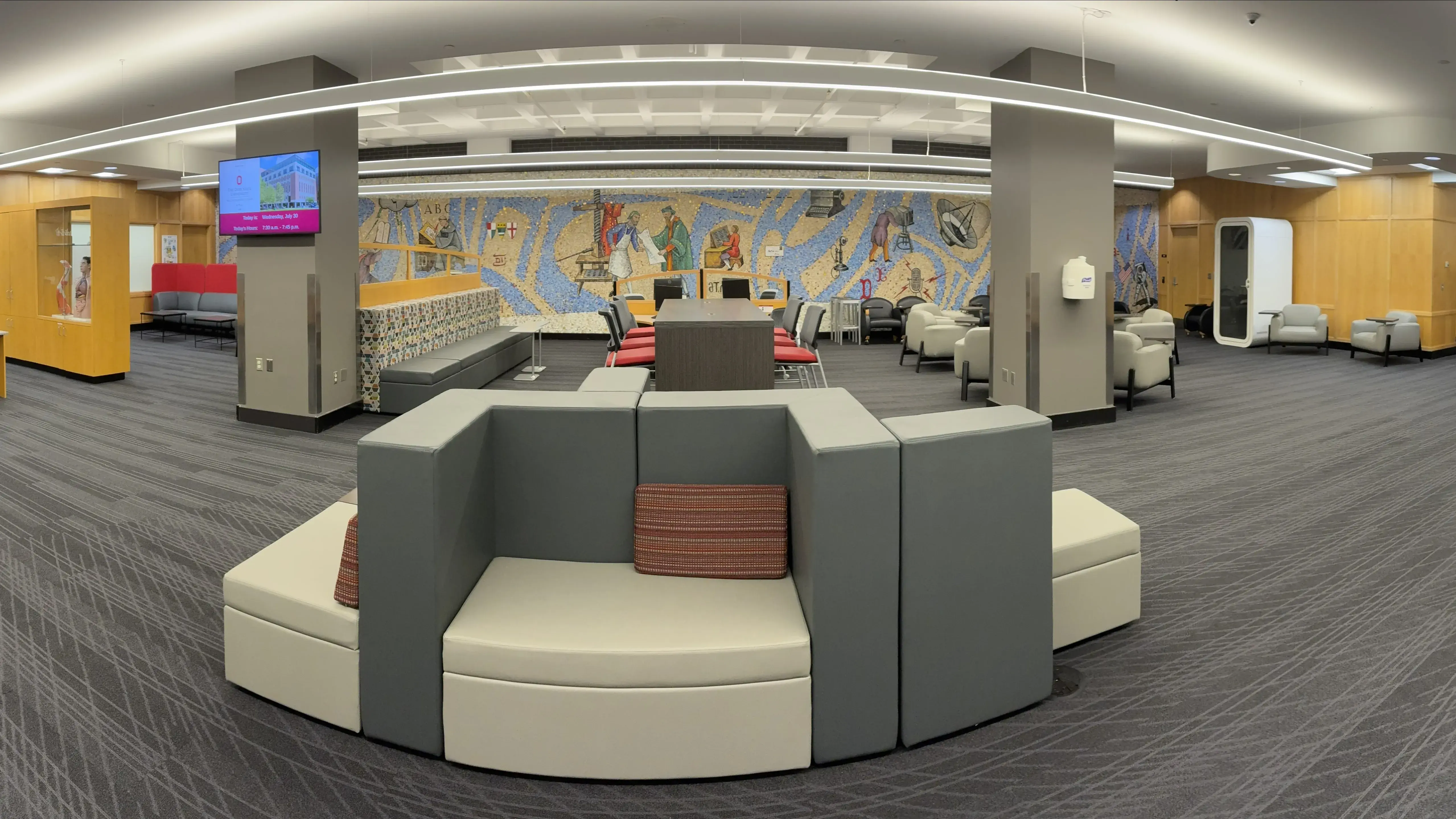 Large library space featuring modern seats, a mosaic wall, info desk, and study zones. Bright lights and neutral colours make it inviting.