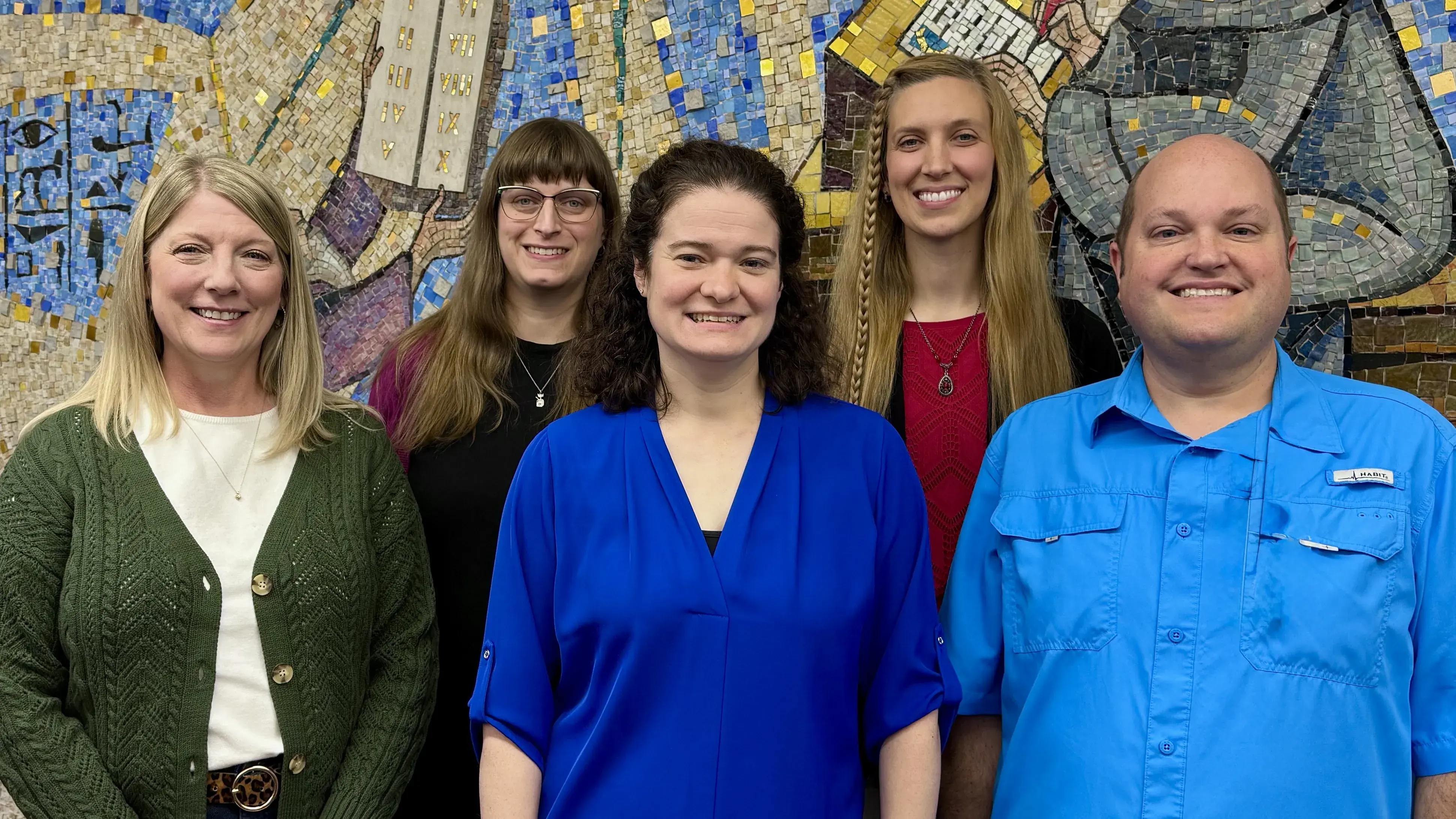 A group of individuals posing in front of a wall mural