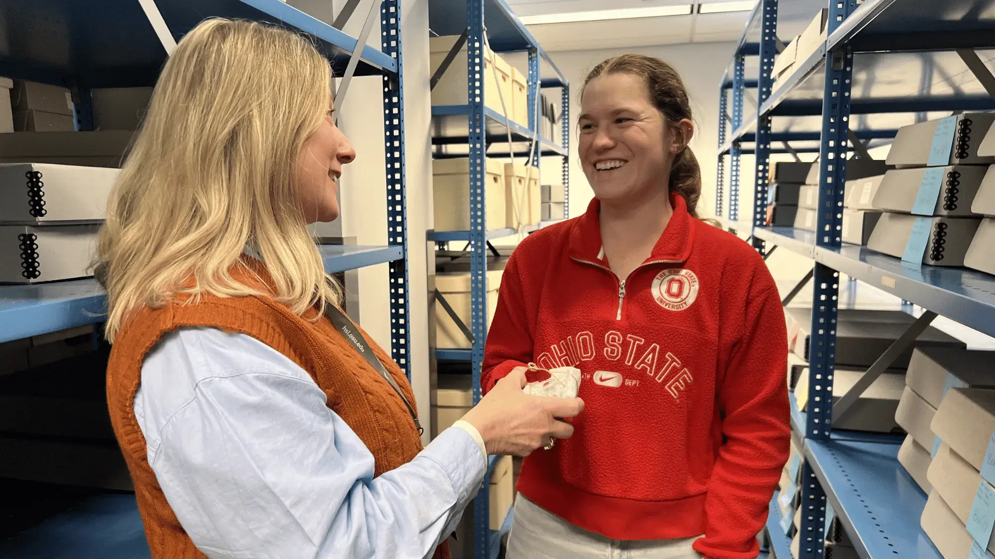 Two women smiling at each other, surrounded by archives.